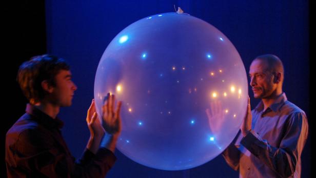 Zwei Männer halten einen großen, leuchtenden Ballon.