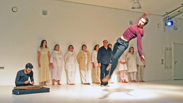 Ein Mann springt vor einer Gruppe von Menschen, während ein anderer ein Saiteninstrument spielt.