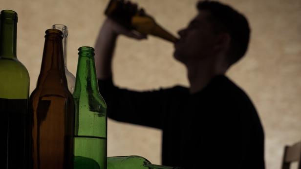 Eine Person trinkt aus einer Bierflasche, umgeben von leeren Flaschen.