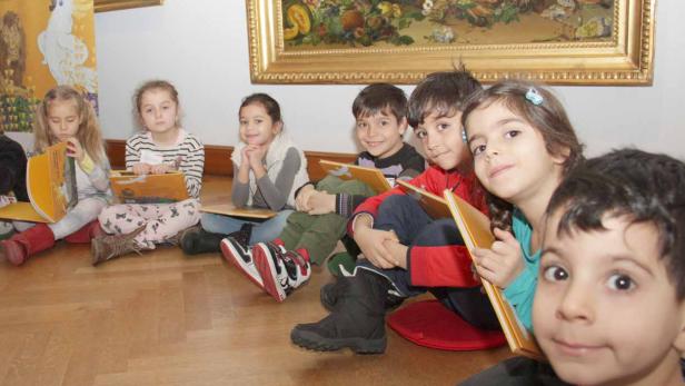 Kinder aus dem Wiener Kindergarten in der Argentinier Straße mit Büchern vor jenem Gemälde von Johann Knapp, in dem sich ein Kakadu befindet.