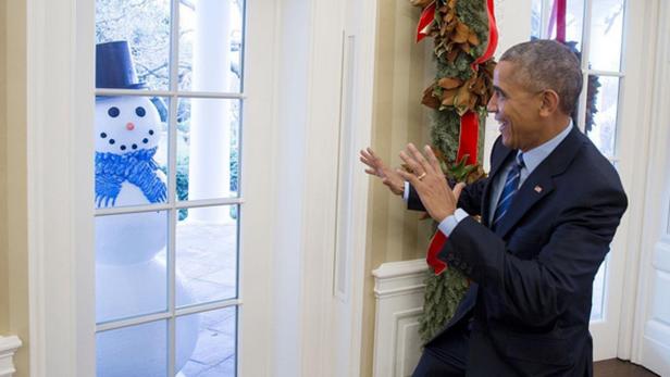 Barack Obama gestikuliert in Richtung eines Schneemanns vor einem Fenster.