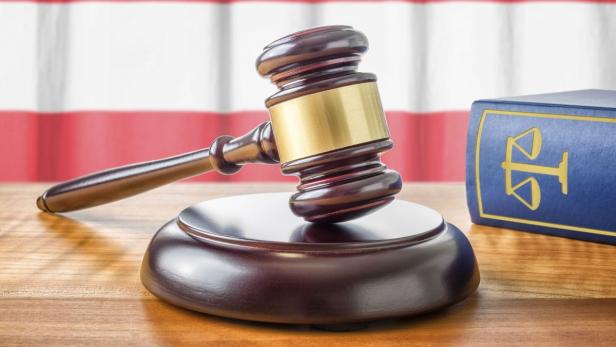 Ein Holzhammer und ein Buch mit einer Justizwaage darauf liegen auf einem Tisch.