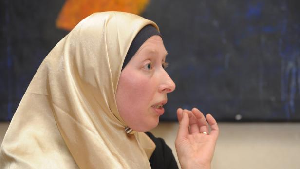 Eine Frau mit hellen Haaren und einem goldenen Hijab spricht.