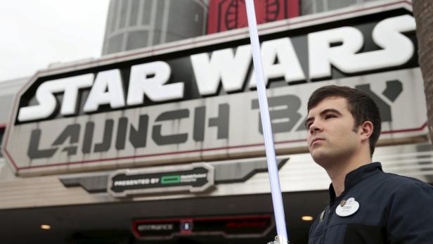 Ein Mann hält ein blaues Lichtschwert vor dem „Star Wars Launch Bay“-Eingang.