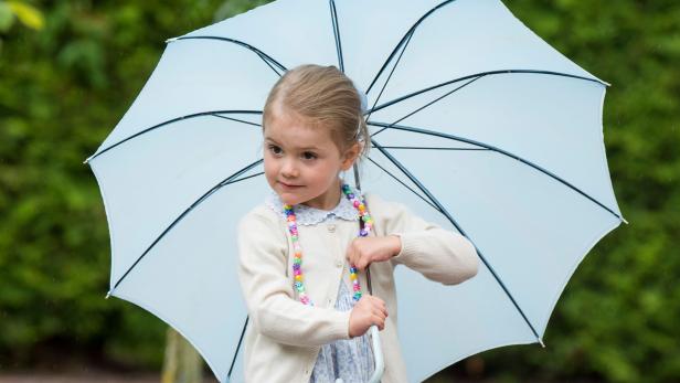 Ein kleines Mädchen steht mit einem hellblauen Regenschirm im Regen.