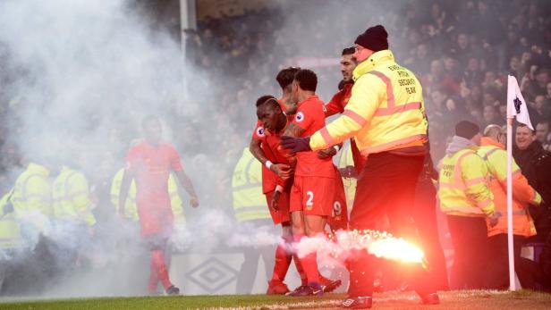 Fußballspieler in roten Trikots feiern inmitten von Rauch und einem bengalischen Feuer.