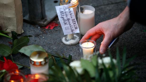 Eine Hand zündet eine Kerze bei einer Gedenkstätte in Berlin an.