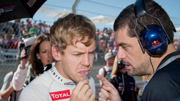 Sebastian Vettel wird von einem Teammitglied im Fahrerlager beraten.
