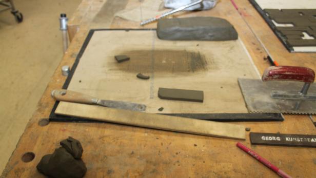 Ein Arbeitstisch mit Ton, Werkzeugen und einer Inschrift „Georg Kunststat“.