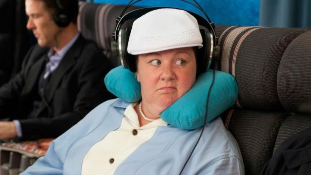 Eine Frau mit Kopfhörern und Nackenkissen sitzt im Flugzeug.