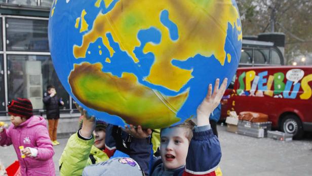Kinder tragen eine große, bemalte Weltkugel auf einer belebten Straße.
