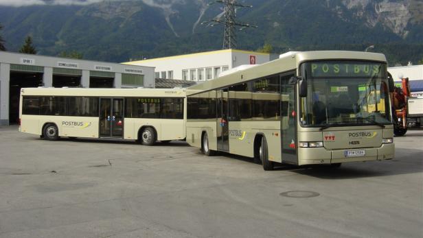 Ein Postbus-Gelenkbus steht vor einem Gebäude mit der Aufschrift „Schnellservice“.