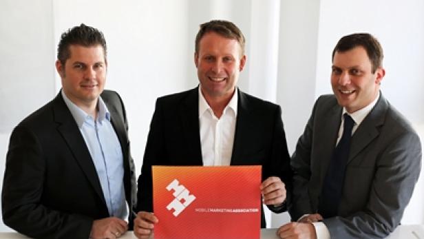Drei Männer in Anzügen präsentieren ein Schild der Mobile Marketing Association.