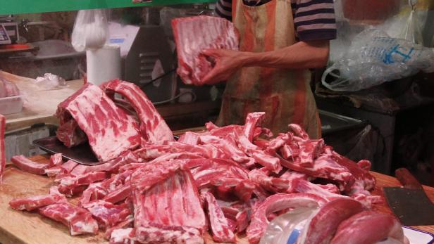 Ein Metzger hält ein Stück rohes Fleisch über einem Stapel Rippchen.