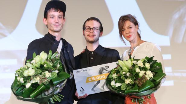 Drei Personen posieren mit Blumensträußen und einem Preisgeld-Scheck über 5.000 Euro.