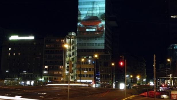 Ein roter Ford Focus wird nachts auf ein hohes Gebäude projiziert.