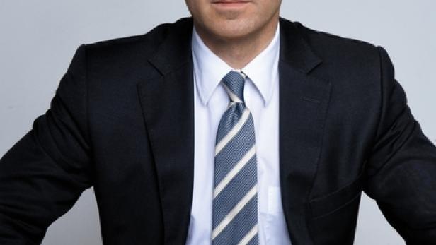 Ein Mann mit dunklen Haaren trägt einen Anzug und eine gestreifte Krawatte.