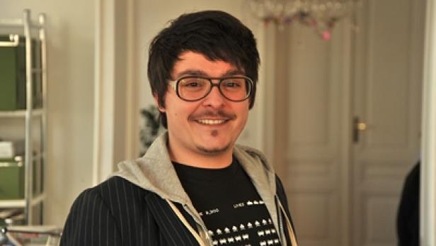 Ein Mann mit Brille und einem T-Shirt mit Space-Invaders-Motiv lächelt in die Kamera.