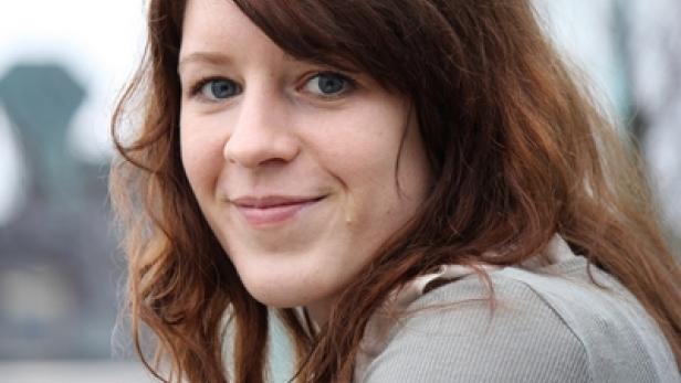 Eine lächelnde Frau mit braunen Haaren und blauen Augen blickt in die Kamera.
