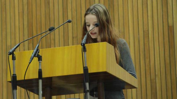 Eine junge Frau steht an einem Rednerpult und spricht in ein Mikrofon.