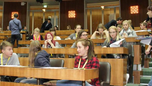 Eine Gruppe Jugendlicher sitzt in einem holzvertäfelten Raum mit Tischen und Stühlen.