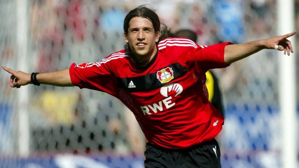 Ein Fußballspieler im roten Trikot von Bayer Leverkusen jubelt mit ausgestreckten Armen.