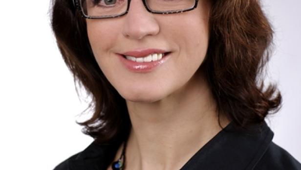 Eine Frau mit braunen Haaren und Brille lächelt in die Kamera.