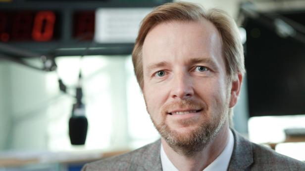 Ein Mann mit blonden Haaren und Bart lächelt in die Kamera.