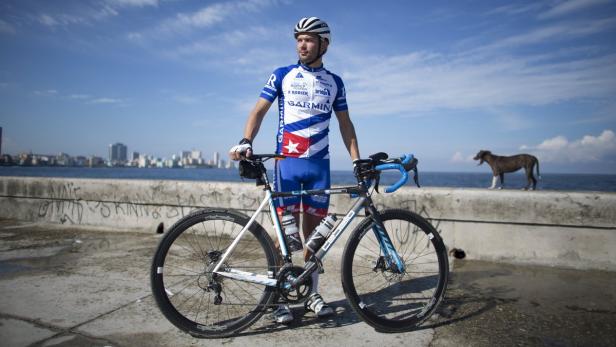 Ein Radfahrer in kubanischer Sportbekleidung posiert mit seinem Fahrrad vor der Skyline von Havanna.