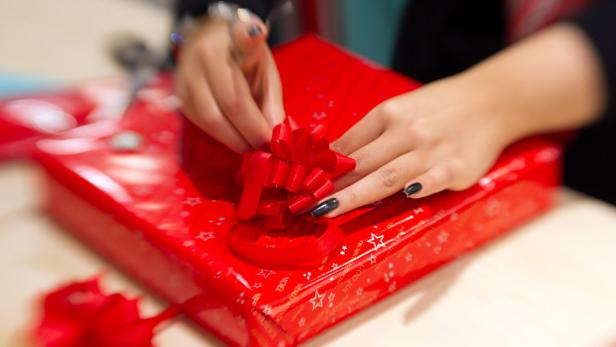 Eine Person bindet eine rote Schleife um ein rot verpacktes Geschenk.