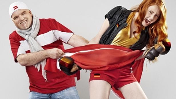 Ein Mann mit Lettland-Trikot und eine Frau im Deutschland-Outfit ziehen an einer Flagge.