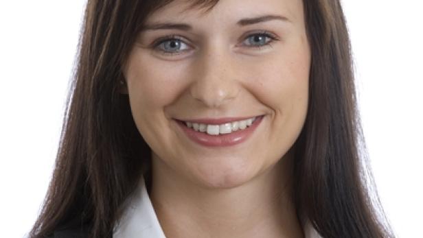 Eine lächelnde Frau mit dunklen Haaren, gekleidet in Bluse, Weste und Perlenkette.