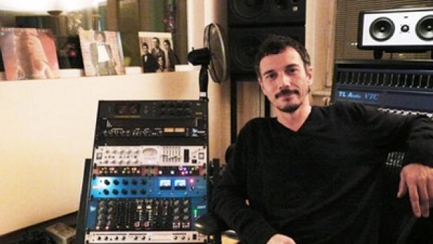 Ein Mann sitzt in einem Musikstudio vor Mischpulten und Lautsprechern.