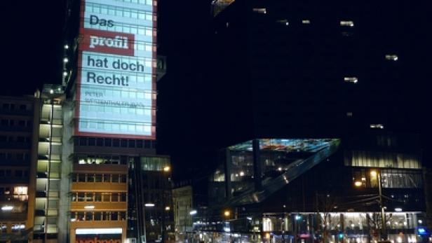 Ein Hochhaus in Berlin ist nachts mit dem Schriftzug „Das profil hat doch Recht!“ beleuchtet.