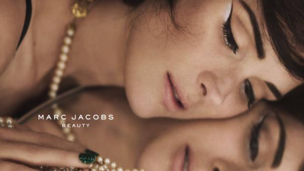 Eine Frau mit Perlenkette und grünen lackierten Nägeln spiegelt sich in einem Spiegel.