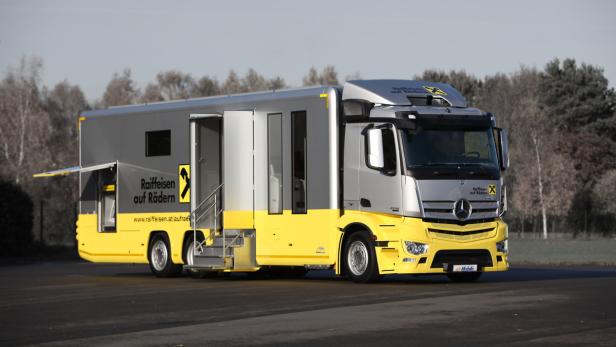 Ein silber-gelber Raiffeisen-Truck mit geöffneten Türen steht auf einem Parkplatz.