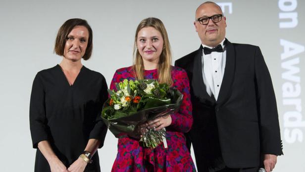 Drei Personen posieren mit einem Blumenstrauß bei einer Preisverleihung.