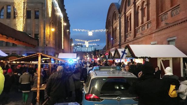 Ein belebter Weihnachtsmarkt mit Menschen, Ständen und einem Polizeiauto im Vordergrund.