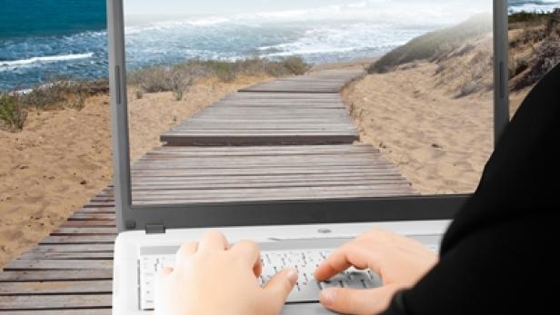 Eine Person arbeitet am Laptop; auf dem Bildschirm ist ein Strand mit dem Schriftzug „Atanango“ zu sehen.
