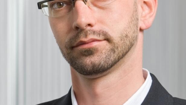 Ein Mann mit Brille, Anzug und Bart schaut in die Kamera.