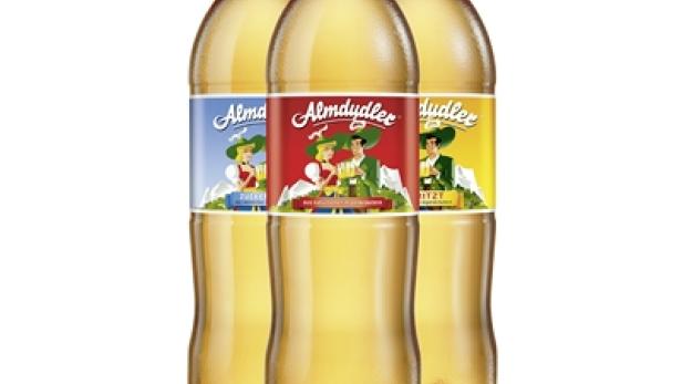 Drei Flaschen Almdudler mit blauen, roten und gelben Etiketten stehen nebeneinander.