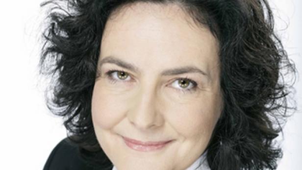 Porträt einer Frau mit dunklen, lockigen Haaren und einem schwarzen Blazer.