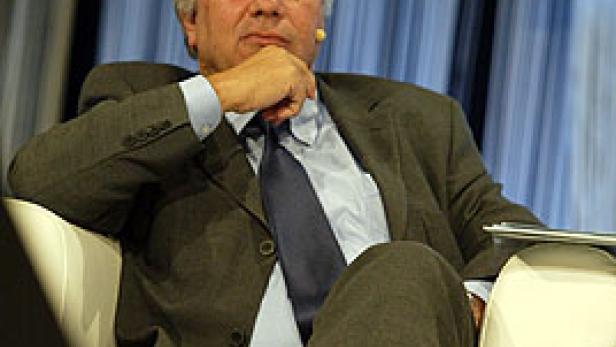 Ein Mann im Anzug sitzt in einem Sessel und blickt in die Kamera.