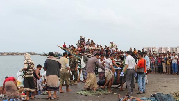 Viele Menschen versammeln sich an einem Hafen, einige auf Booten, andere am Ufer.