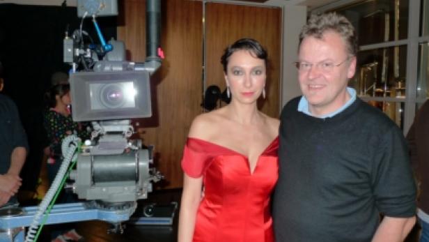 Eine Frau in einem roten Kleid posiert mit einem Mann vor einer Filmkamera.