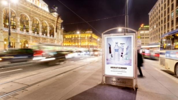Ein Absolut Vodka Werbeplakat steht an einer belebten Straße in Wien bei Nacht.