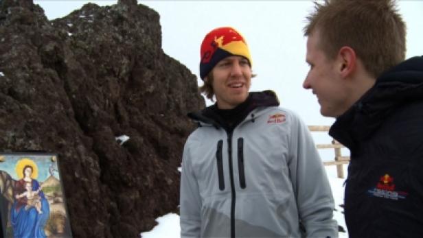 Sebastian Vettel steht mit einer anderen Person vor einem Felsen und einem Marienbild.