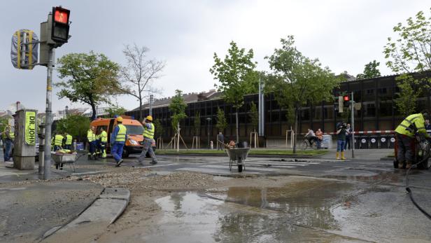 Bauarbeiter reparieren eine Straße mit einer Wasserlache in einer städtischen Umgebung.