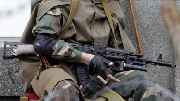 Ein Soldat in Tarnkleidung sitzt mit einem Gewehr im Schoß.