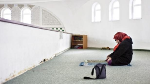 Eine Frau mit Kopftuch betet in einer Moschee auf einem Gebetsteppich.
